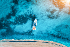 Aerial view of the white yacht in the clear blue water at sunset in summer. Top view from drone of boat, sandy beach. Indian ocean. Travel in Zanzibar, Africa. Tropical landscape with motorboat, sea