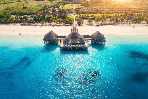 Aerial view of beautiful hotel in Indian ocean at sunset in summer. Zanzibar, Africa. Top view. Landscape with wooden hotel on the  sea, blue water, sandy beach, green trees, buildings. Luxury resort