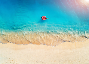 Aerial view of a young woman swimming with the donut swim ring in the clear blue sea with waves at sunrise in summer. Tropical aerial landscape with girl, azure water, sandy beach. Top view. Travel