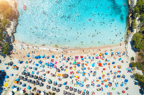 Aerial view of sandy beach with colorful umbrellas, swimming people, sea coast with transparent blue water, green trees at sunset in summer. Travel in Mallorca, Balearic islands, Spain. Top view