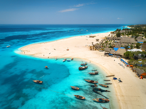 Aerial view of the fishing boats on tropical sea coast with sandy beach at sunny day. Summer holiday on Indian Ocean, Zanzibar, Africa. Landscape with boat, buildings, transparent blue water. Top view