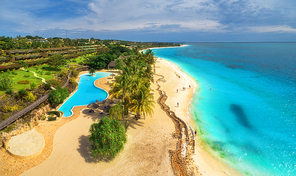Aerial view of sea coast. Sandy beach with pool, palms and umbrellas at sunset. Summer holiday on Indian Ocean, Zanzibar, Africa. Tropical landscape with palm trees, hotels, sand, blue water. Top view