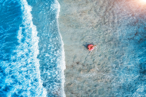Aerial view of a young woman swimming with the pink donut swim ring in the clear blue sea with beautiful waves at sunset in summer. Tropical aerial landscape with girl, azure water. Top view. Travel