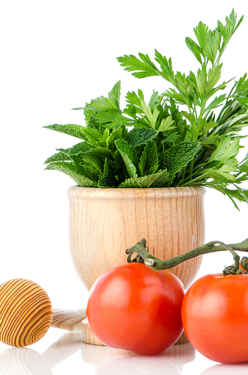 Tomatoes on the vine and green herb leafs sprigs in an wood mortar over white background.
