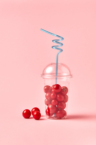 Big plastic glass with organic fresh miniature tomatoes - ripe red vegetables on a pink paper background. Place for text. Concept of detox healthy eating.