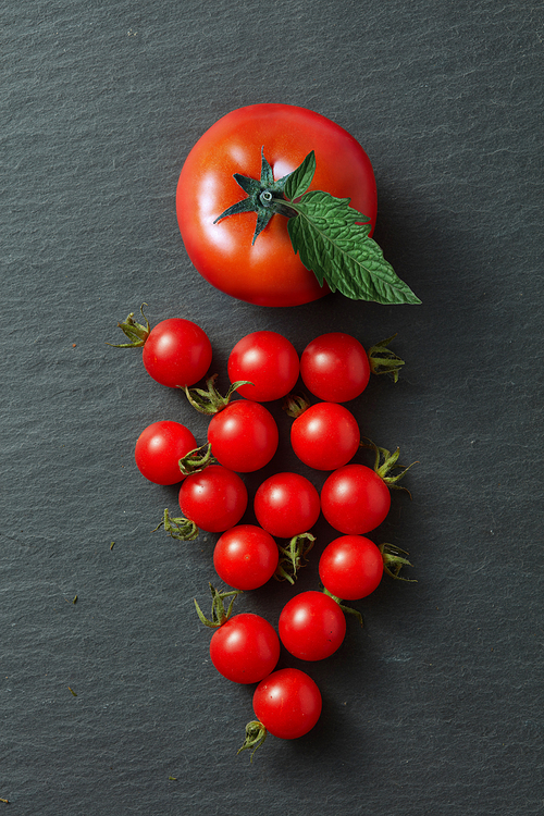 bunch of cherry tomatoes with leaves isolated on a black concrete background