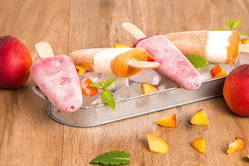 Homemade raspberries and peach popsicles on a wooden table.