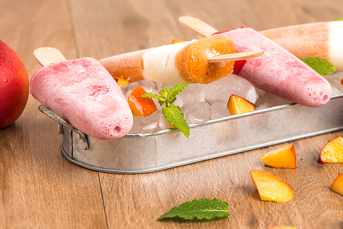 Homemade raspberries and peach popsicles on a wooden table.