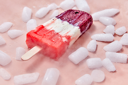 Fruit popsicle. Sweet, berry homemade ice cream on a stick with slices of ice on a pink background. Summer dessert