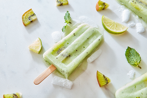 Fruit frozen juice lolly. Summer composition of a refreshing ice cream with ice, mint leaves, pieces of kiwi and lime on a gray marble background with space for text. Flat lay