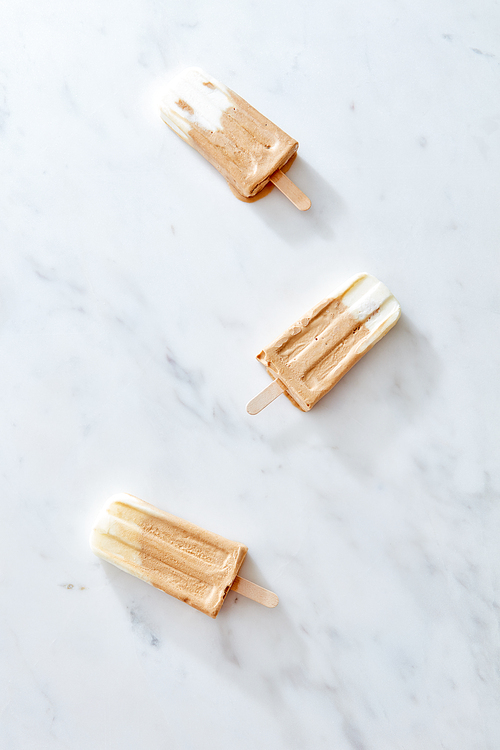 Frozen coffee gelato ice cream on a wooden stick over marble background, top view. Summer delicious desserts