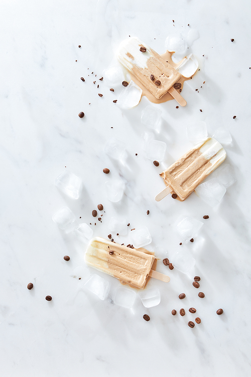 Homemade coffee ice cream with caramel and coffee beans on a wooden stick over marble and ice background, top view