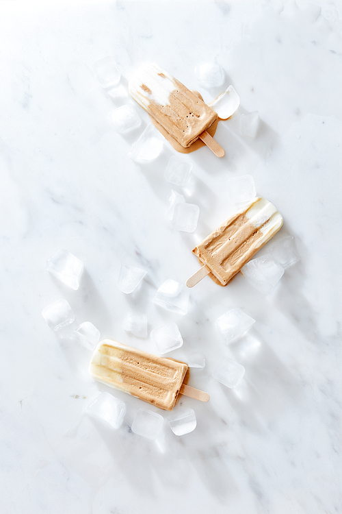 Three creme brulee coffee ice creams on a wooden stick over marble background, top view. Healthy summer dessert