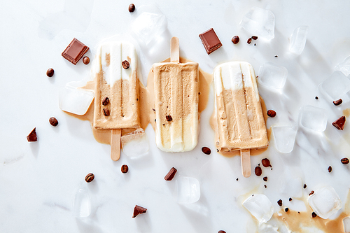 Vegan banana coffee creamy dairy free ice popsicles over ice and marble background with piece chocolate and coffee beans, top view