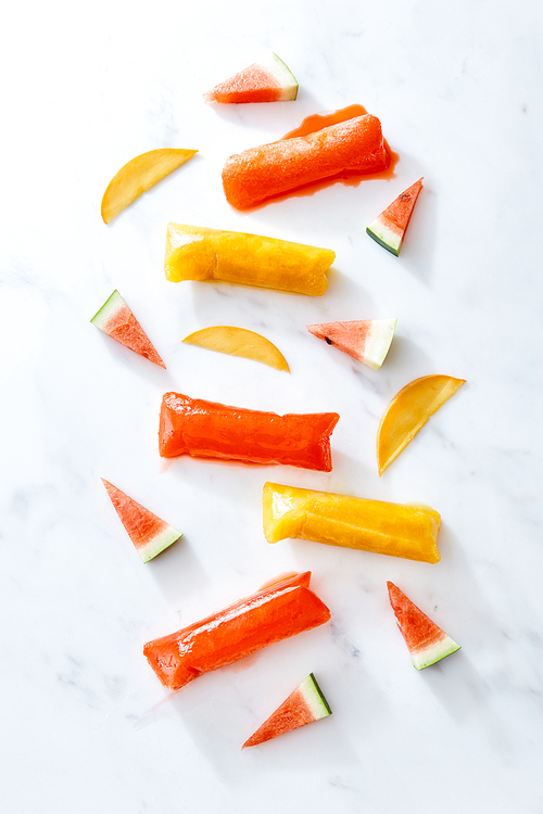 Freeze ice pop plastic tube for popsicle packaging with slice watermelon and peach on marble background, top view. Healthy summer dessert