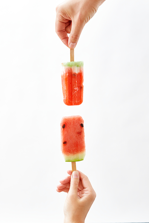 A girl's hand holds fresh organic slices of watermelon on a stick on a white background with copy space. The concept of summer cold dessert. Ice lolly