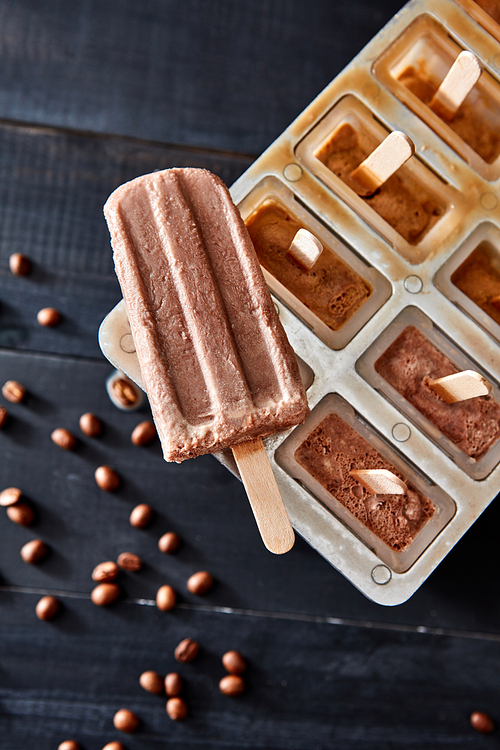 Homemade popsicles with chocolate on ice cube container with coffee beans on dark wooden background, flat lay. Homemade prepare concept