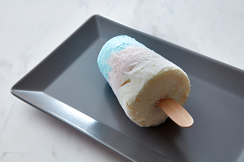 Close-up colored appetizing ice cream lolly in a black plate on a gray marble background with copy space. A summer dessert. Flat lay