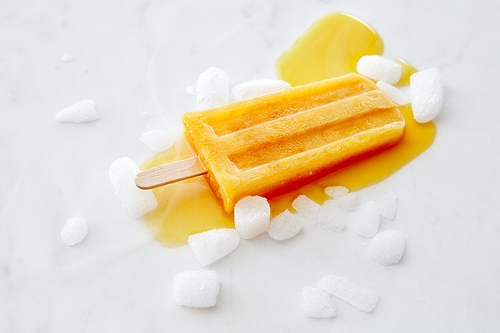 Orange melting ice cream lolly with ice slices on a gray marble table with a copy of the space. The concept of summer dessert.Flat lay
