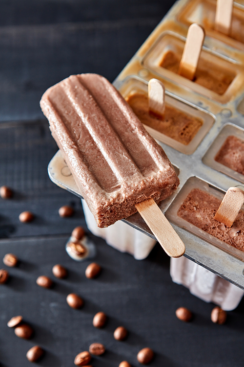 Natural coffee ice cream popsicle with coffee beans presented on a black wooden table. Summer dessert. Top view