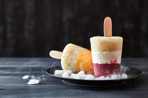 Fruit coffee homemade ice cream lolly on a stick in a black plate with slices of ice on a wooden dark table with copy space. Cold dessert