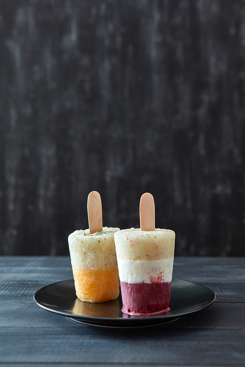 Various coffee, fruit homemade ice popsicle presented in a black plate on a dark wooden background with space for text. Cold dessert