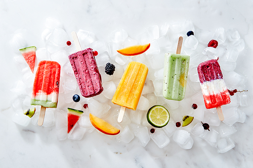 Collection of colorful tasty homemade ice cream lolly on a stick with juicy berries and pieces of various fruits on ice cubes. Flat lay
