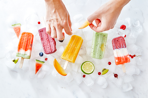 Fruit berry ice lolly on ice cubes. A woman's hand decorates ice cream with pieces of fresh fruit fruit. Flat lay