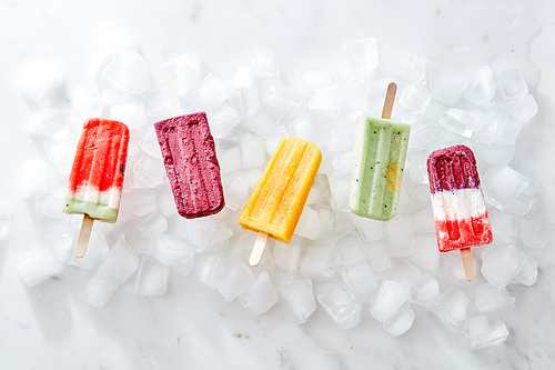 Different fruit ice cream popsicle presented on ice cubes on a gray marble background. Flat lay