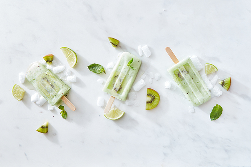 Set of ice cream on a stick with kiwi, mint and lime on a gray marble background with pieces of ice and fruit. Space for text. Flat lay
