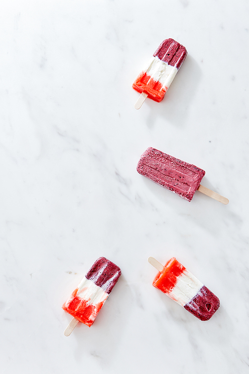 A healthy fruit colored ice cream on a stick on a gray marble table with a copy of the space for text. Summer dessert. Flat lay