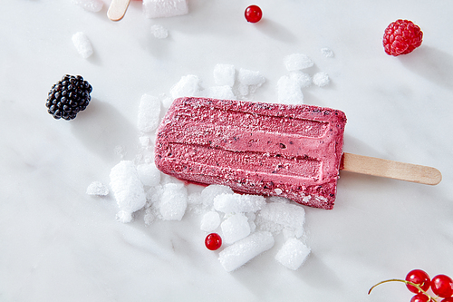 Berry apetitic organic ice cream lolly is represented on a gray marble table with different berries and ice cubes with a copy of the space