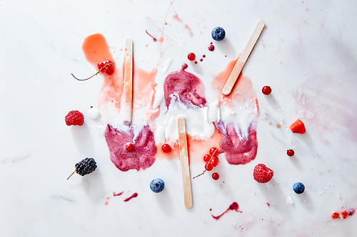 Multicolored splashes of melted ice cream sticks and juicy berries of raspberries, blueberries, blackberries and red currants on a gray marble background with space for text.