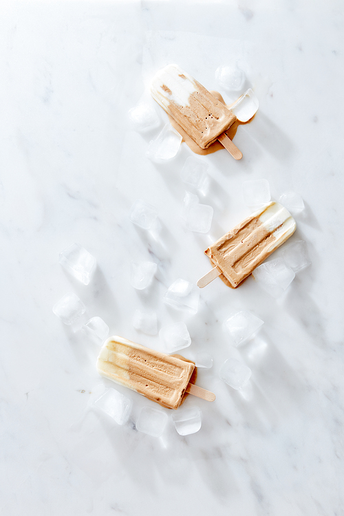 Sweet creamy coffee ice cream on a stick with ice cubes in a gray marble table with space for text. Homemade refreshing dessert. Flat lay