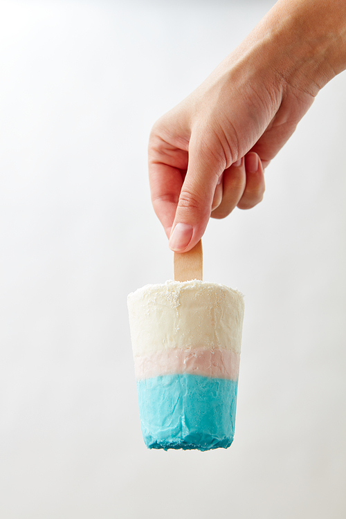 A white blue ice cream on a stick holds a female hand on a gray background with a copy space. Sweet cold dessert