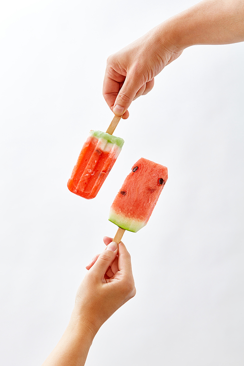 Creative food composition of a fruit ice cream in a female hand and a juicy piece of watermelon on a stick holds a male hand on a gray background space for text. Summer dessert