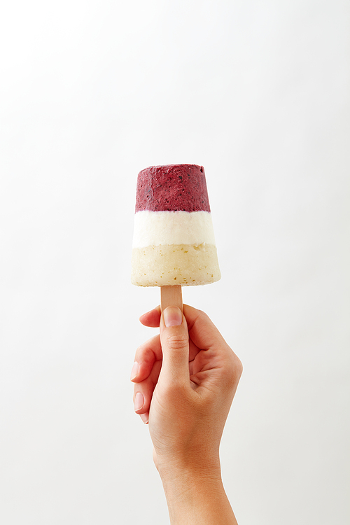 Berry sorbet lolly. The girl's hand holds an ice cream on a gray background with space for text. Sweet cold dessert
