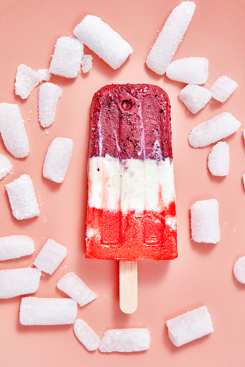 Fruit homemade colored ice cream on a stick with cold ice cubes on a color background of the year 2019 Living Coral Pantone. Cold dessert. Top view