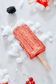 Homemade popsicle blueberry and cream in color of the year 2019 Living Coral Pantone on crushed ice over a marble background with berries, top view. Summer concept