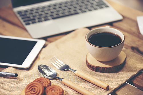 Digital tablet and cup of coffee on old wooden desk. Simple workspace or coffee break in morning/ selective focus