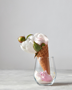 Sweet waffle cone with beautiful white peony flower and petals in a glass cup on a gray background with copy space. Summer concept of congratulations for Valentine's Day