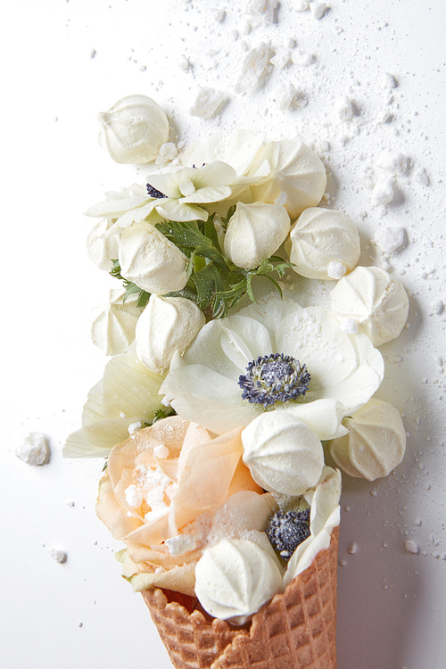 Ice cream of white flowers in waffle cone with meringues on white background from above, flat lay styling