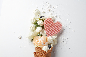 Beautiful flower in ice cream cone with meringues and waffle heart on a white background