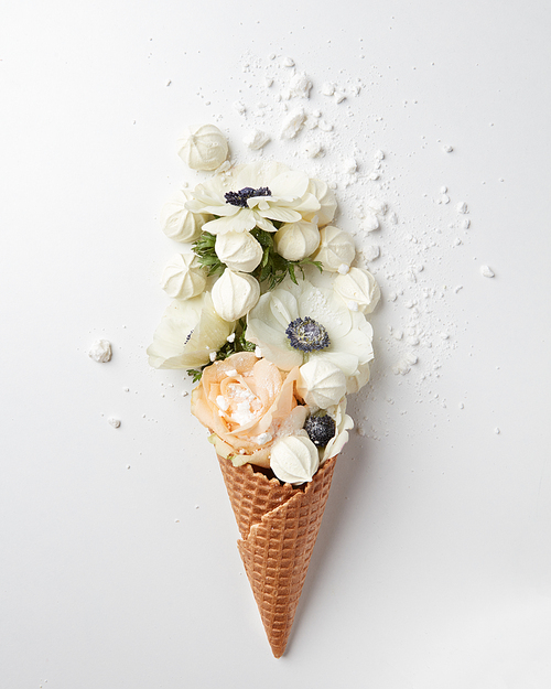 waffle cone with flowers bouquet and meringues on white background, flat lay, top view