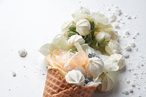 Waffle cone with bouquet of beautiful flowers with meringues on white background