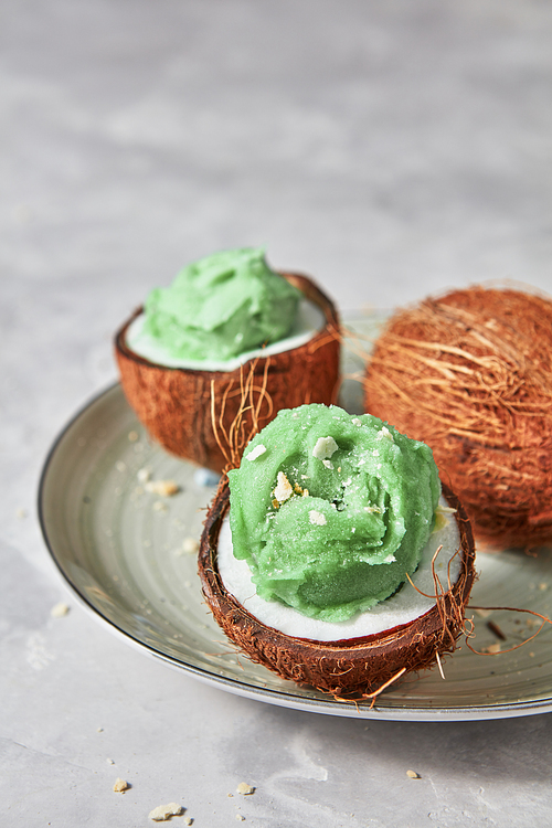 Fresh green mint ice cream in coconut shell with whole fresh coconut on a plate on a gray concrete, copy space. Summer concept for vegan eating