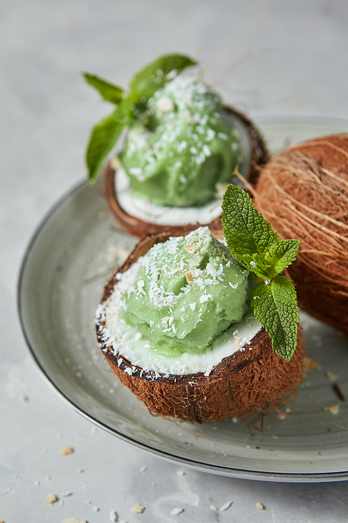 The coconut with green frozen mint dessert, green mint leat on a plate on a gray background. Summer food concept for vegan eating.