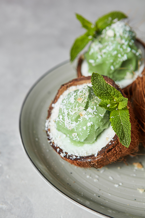 Mint green ice cream homemade in a coconut shell on a gray concrete background with place for text. Summer dessert for vegetarian eating