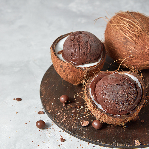 Two halves of coconut with homemade chocolate dessert on a wooden board on a gray background with copy space.. Summer concept.