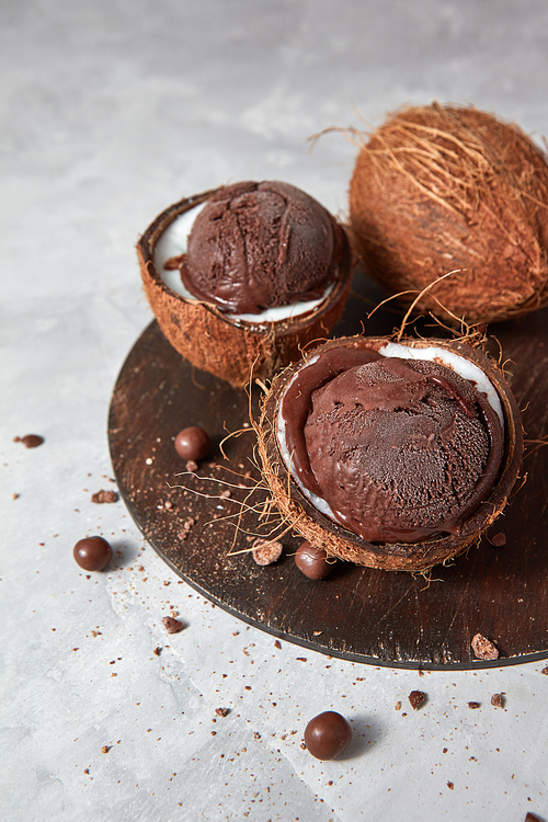 Delicious chocolate sorbet in a coconut shell on a wooden board on a gray concrete background with place for text. Vegetarian concept of diet eating